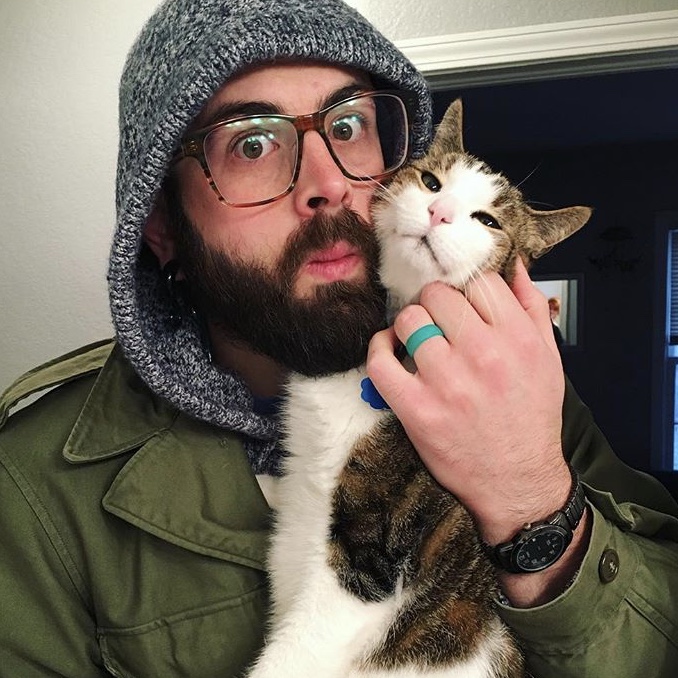 Joe is wearing his winter coat while snuggling Nibbler, a tabby cat with a predominantly white face and belly.